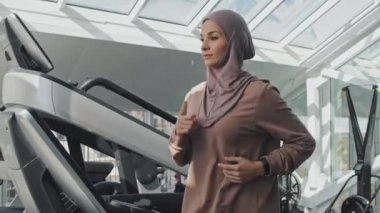Spor yaparken koşu bandında koşan tesettürlü genç Müslüman kadın.