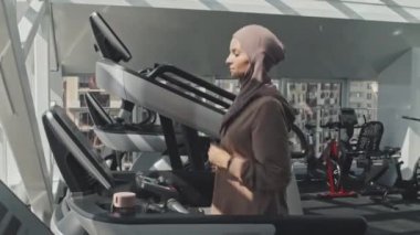 Spor yaparken koşu bandında koşan tesettürlü genç Müslüman kadın.