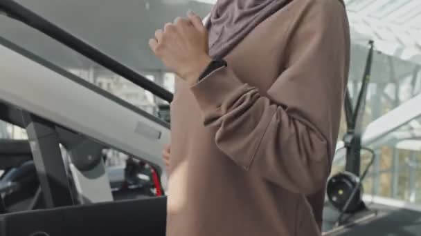 ティルトアップショットの美しいですイスラム教徒女性でヒジャーブランニング上のトレッドミルでジムトレーニング中 — ストック動画