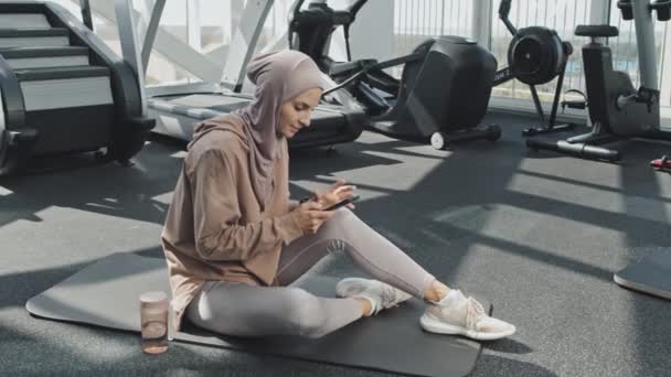 Junge Muslimin Hidschab Und Sportbekleidung Sitzt Fitnessstudio Auf Gymnastikmatte Und — Stockvideo