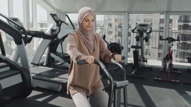Spor kıyafetleri ve tesettürlü Müslüman kadını spor salonunda bisiklet egzersizi yaparken çek.