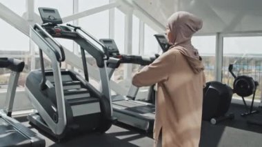 Spor kıyafetleri ve tesettürlü Müslüman bir kadın spor salonunda antrenmandan önce ısınırken gövde rotasyonu yapıyor.