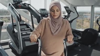 Spor salonunda bisiklet egzersizi yaparken kırtasiye bisikleti üzerinde egzersiz yapan tesettürlü güzel Müslüman kadın.