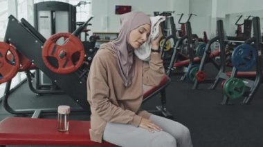 Havluyla yüzünü silen, spor yaptıktan sonra kameraya bakıp gülümseyen güzel Müslüman kadın portresi.