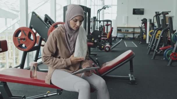 Junge Muslimin Hijab Und Sportbekleidung Sitzt Auf Bank Fitnessstudio Wischt — Stockvideo