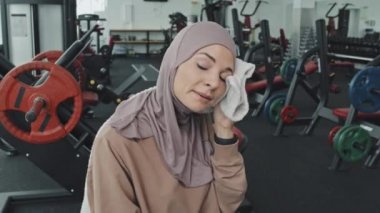 Kafiyeli genç Müslüman kadın portresi havluyla yüzünü siliyor spor salonundan sonra dinlenirken kameraya gülümsüyor.