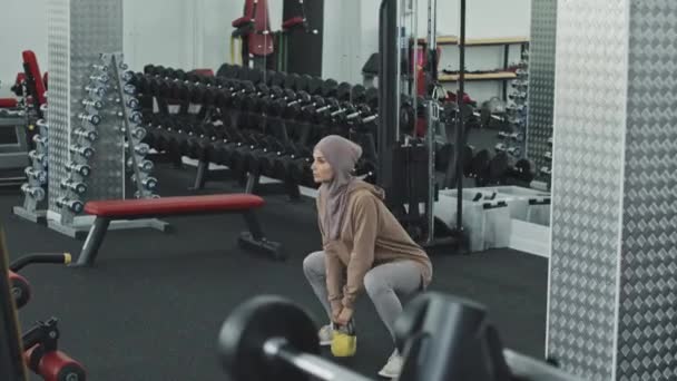 ヒジャーブ州のイスラム教徒の女性とスポーツウェアをやって重みのあるスクワットとともにケトルベル体操中 — ストック動画