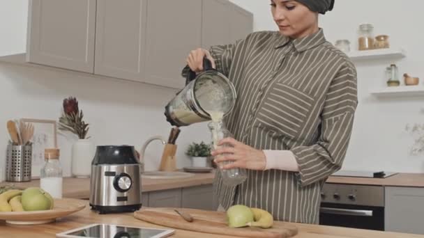 穆斯林妇女头戴头巾 把新鲜的冰沙从搅拌机倒进家里厨房的瓶子里 — 图库视频影像