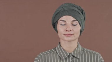 Başörtülü genç Müslüman kadının stüdyo portresi gözleri kapalı kameraya bakıyor.