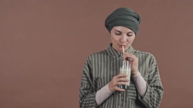 Türbanlı güzel Müslüman kadın portresi. Taze smoothie içiyor ve stüdyoda poz verirken kameraya gülümsüyor.