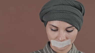 Başörtülü Müslüman bir kadının portresi. Ağzındaki bandı çıkarıyor ve stüdyoda kameraya gülümsüyor.