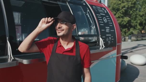 黒キャップで笑顔若い男の中肖像画とエプロン笑顔でカメラスタンド外に赤いトラックの横にある晴れた日に食べ物 — ストック動画