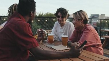 Sıcak bir yaz akşamında çatıdaki kafede oturup sohbet eden dört etnik kökenli hippi arkadaşın orta boy fotoğrafı.