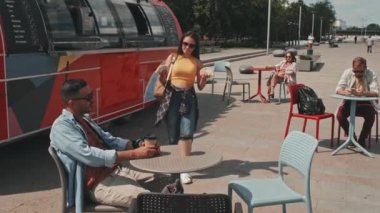 Genç bir çiftin güneşli bir günde sokak yemekleri kamyonuyla açık kafedeki plastik masada oturup kahve eşliğinde taco yerken ve sohbet ederken orta boy fotoğrafı.