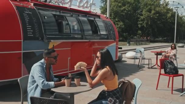 赤いトラックで屋外のカフェに座っている間 若い出産のカップルはタコスを食べて会話をしています — ストック動画