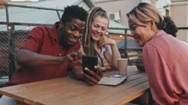 Yazı dışarıda, çatıdaki kafede birlikte geçirdikleri akıllı telefonlara bakıp gülen orta sınıf genç arkadaşlar.