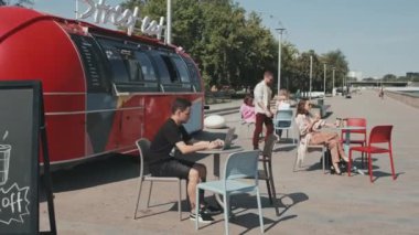 Yazın güneşli bir günde Red Street yemek kamyonunun yanındaki açık kafede oturan insanlar.
