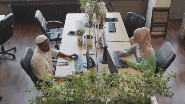 若いイスラム教徒の白人女性と黒人男性の高い角度は 職場では反対側の机に座って コンピュータを使用して — ストック動画