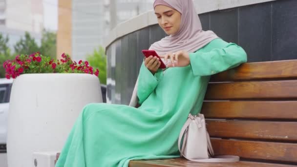 Tilting Young Muslim Woman Wearing Hijab Sitting Bench Outdoors Texting — 图库视频影像