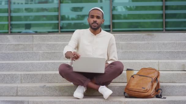Full Shot Young Black Man Wearing Kufi Closing Laptop Computer — стоковое видео