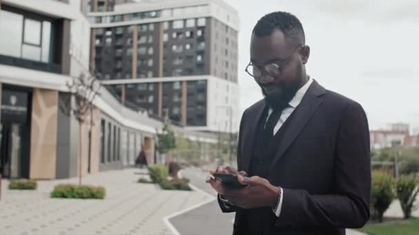 Nyomkövető Felvétel Afro Amerikai Üzletemberről Öltönyben Szemüvegben Kint Áll Mobiltelefont — Stock videók