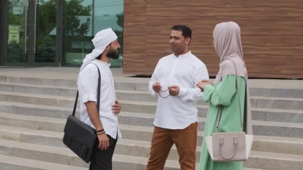 都市の近代的な建物の外に立って若い多民族のイスラム教徒の女性と男性の中長い話と笑顔 — ストック動画