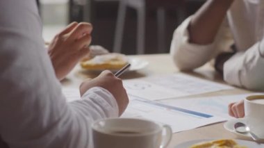 Kafedeki masada oturan, kahve içen, belgelerle uğraşan, iş görüşmeleri yapan tanınmayan dört meslektaşın düşük açılı elleri.