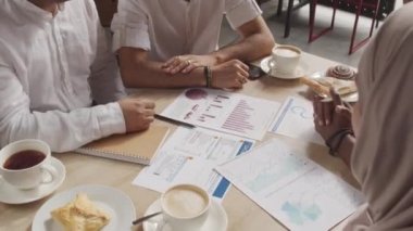 Kafedeki masada oturan, kahve içen, molada belgelerle uğraşan, el sıkışan dört erkek ve kadının yüksek açılı görüntüsü.