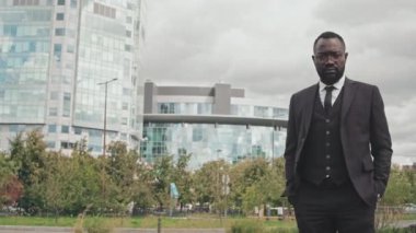 Şehirde kameraya poz veren üç parçalı takım elbiseli zarif Afro-Amerikan iş adamının portresi. Arkaplanda binalar