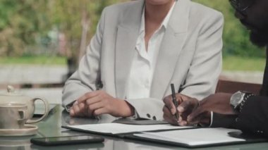 Asyalı iş kadını ve Afro-Amerikalı iş adamının açık kafede oturup kontrat imzalarken, el sıkışırken ve anlaşma yaparken orta bölüm çekimi.