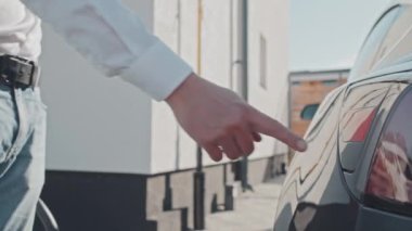 El bilgisayarı orta bölüm takibi. Şarj istasyonunda elektrikli arabasını şarj eden tanınmayan bir adamın elleri kapalı.