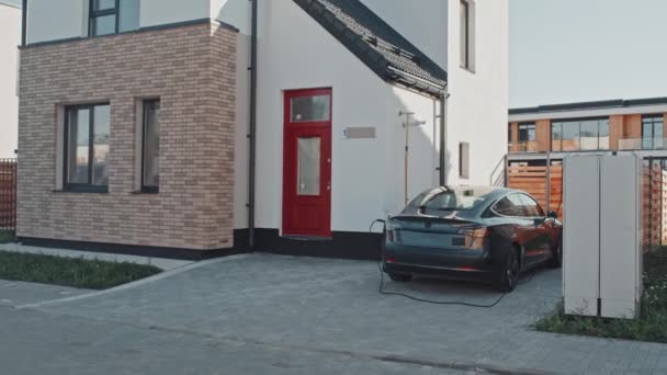 郊外の家の前に停まっている間の電気自動車充電の手持ち追跡 — ストック動画