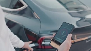 Şarj etmek için elektrikli araba takan ve cep telefonu uygulaması kullanan tanınmayan bir adamı kapatın.