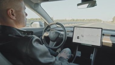 Otobanda kendi kendine giden elektrikli arabanın arka koltuğundan çekilen el kamerası. Şoför koltuğunda oturan adam.