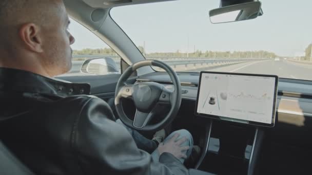 高速道路を走行する自家用電気自動車の後部座席から手持ち撮影 運転席に座っている男 — ストック動画
