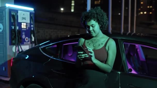 Śledzenie Ujęcia Wesołej Młodej Afroamerykanki Opierającej Się Elektrycznym Samochodzie Stacji — Wideo stockowe
