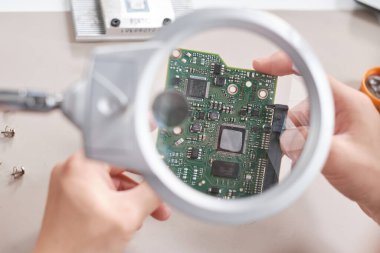 Büyüteç camı ve devre kartı tutan teknisyenlerin elleri