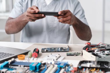 Elektronik cihazın devre kartının fotoğrafını çeken genç Afrikalı tamircinin elleri