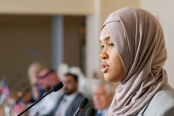 Jovem e bonita oradora no hijab conversando com o público na conferência — Fotografia de Stock