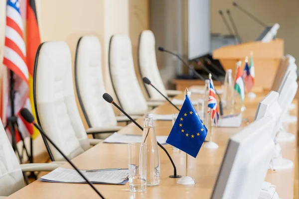 Row of microphones, flags, papers and other on long table in conference hall — Stock Photo, Image