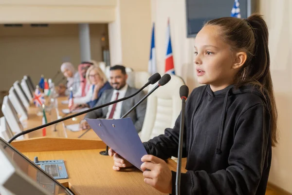 Linda colegiala con portapapeles haciendo informe por tribuna — Foto de Stock