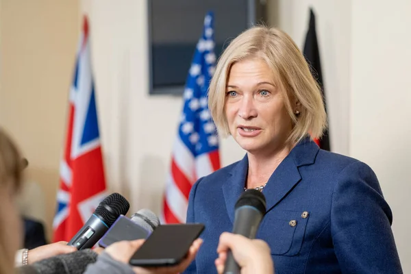 Mature female deputy in elegant suit speaking in microphones of journalists — Stockfoto