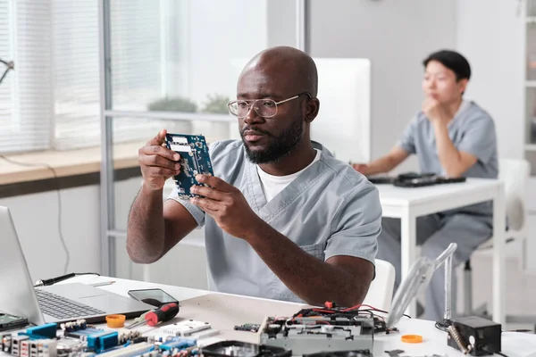 Jonge serieuze reparateur kijkt naar printplaat in zijn handen — Stockfoto