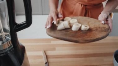 Mutfakta smoothie yaparken kesilmiş muzu miksere koyan genç bir kadının el kamerası.