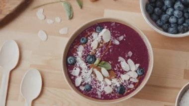 Mutfak masasında duran, ağız sulandıran, badem, hindistan cevizi ve yaban mersinli smoothie kasesini yakından takip edin.