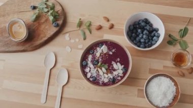 Nefis meyve suyu kasesinin, bademlerin, hindistan cevizi tanelerinin, yabanmersinlerinin, nane ve balın en iyi görüntüsü masanın üzerinde.