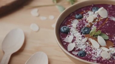 Badem ve hindistan cevizi taneleri, yabanmersini, nane ve kaşık dolusu bal içeren sağlıklı smoothie kasesini yakından takip ediyoruz.