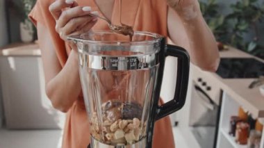 Sabahları smoothie pişirirken incir ve kaju karışımına karabuğday balı ekleyen tanınmayan genç bir kadının el kamerası.