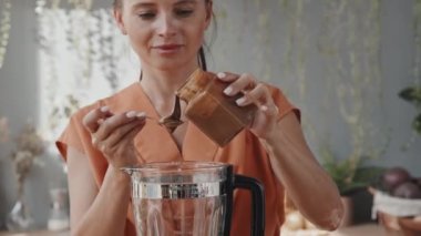 Genç vejetaryen kadının fındıklara kaju ve incirlere kaşık dolusu lezzetli karabuğday balı ekleyip mutfakta smoothie hazırlarken aşağı eğilmesini.