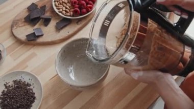 Tanımlanamayan bir kadının içeceği kaseye doldurması. Mutfak tezgahında rendelenmiş çikolata, badem ve ahududu var.